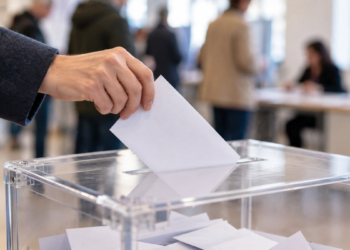 Una mano introduce un sobre electoral blanco en una urna transparente