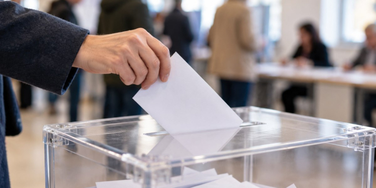 Una mano introduce un sobre electoral blanco en una urna transparente