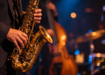 Primer plano de las manos de un músico tocando un saxofón en un concierto de jazz, con instrumentos desenfocados al fondo y sin rostros visibles