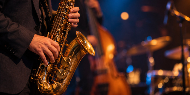 Primer plano de las manos de un músico tocando un saxofón en un concierto de jazz, con instrumentos desenfocados al fondo y sin rostros visibles